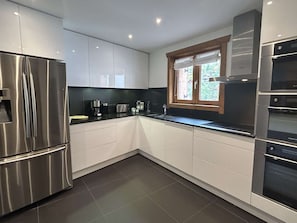 A modern kitchen with stainless steel appliances, white cabinetry, and a window with wooden frames. - Semi-detached chalet, mountain view - 6 guests (Méribel)