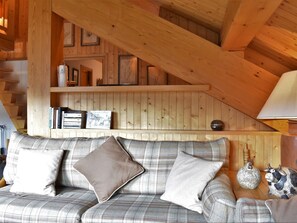 A cozy room with a plaid sofa, a wooden ceiling, and a bookshelf with books and decorative items. - Apartment at the slopes - 8 guests (Méribel)