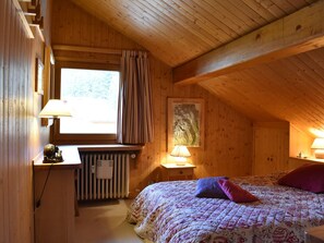 Ein gemütliches Zimmer mit Holzboden, einem Bett mit floralem Bettzeug, einem Heizkörper und einem Fenster mit Vorhängen.