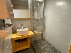 A bathroom with a white sink, a wooden vanity, a glass shower enclosure, and tiled walls. - Charming T2 at the foot of the slopes - 5 guests (Arêches-Beaufort)
