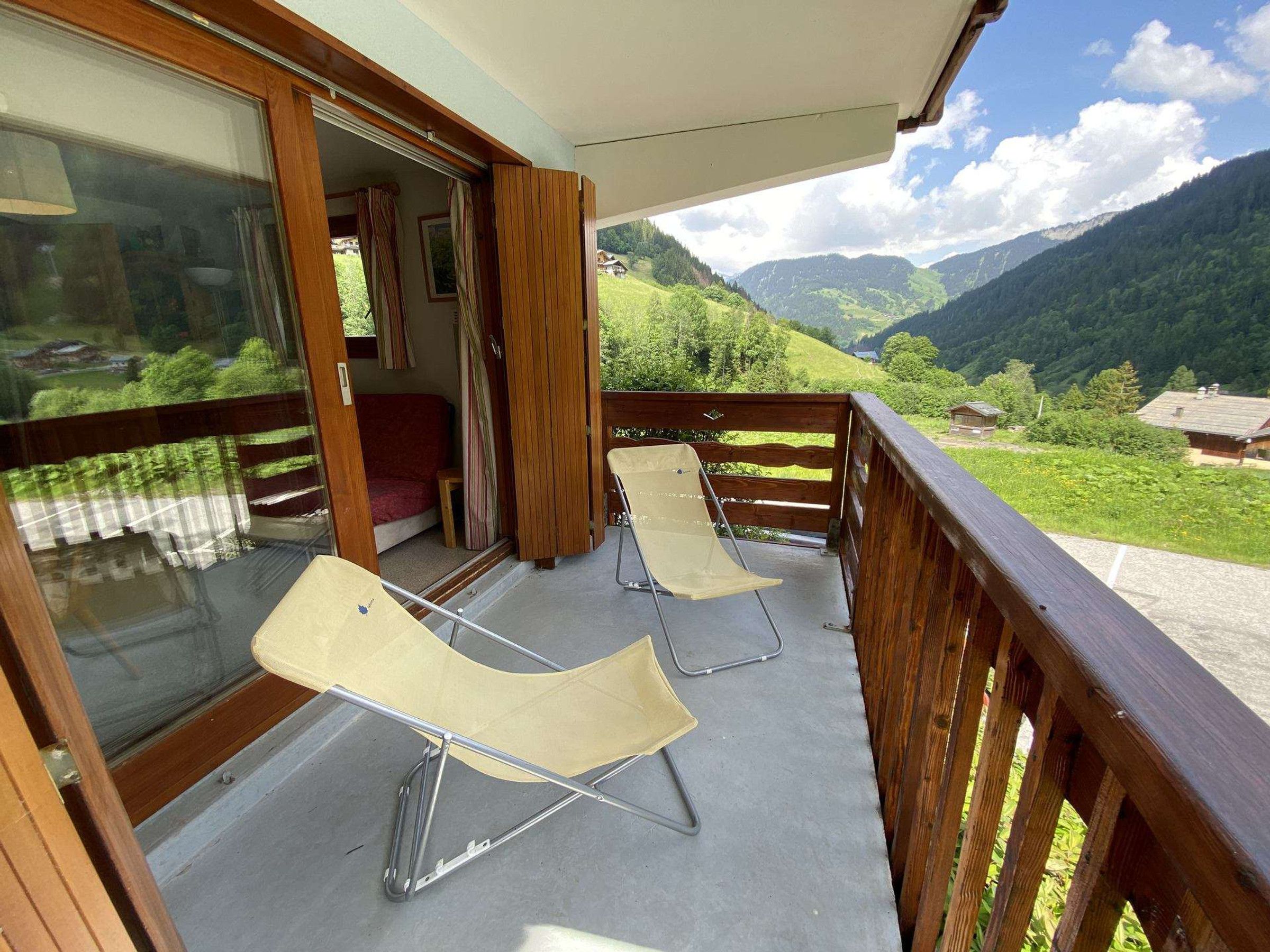 Un balcon avec deux chaises longues, une balustrade en bois et une vue sur un paysage montagneux.
