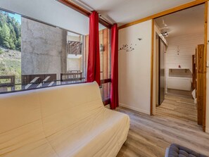 Ein Zimmer mit einer Couch, Blick auf einen Wald durch ein Fenster und einem Badezimmer mit Dusche und Toilette.