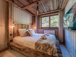 A rustic wooden bedroom with a large bed, a window with a view of greenery, and a wall-mounted light fixture. - New apartment near slopes - 4 guests (Courchevel)