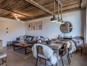A dining area with a rustic wooden ceiling, a round mirror, and a sofa with a fur throw. - New apartment near slopes - 4 guests (Courchevel)