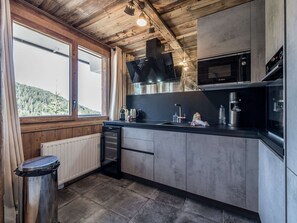 A modern kitchen with a built-in oven, microwave, and a large window offering a view of the outdoors. - New apartment near slopes - 4 guests (Courchevel)