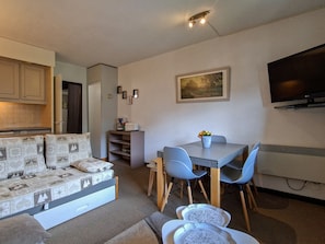 A compact living space with a sofa, a dining table with chairs, a kitchen area, and a flat-screen TV mounted on the wall. - Apartment in Flaine Forêt - 6 guests (Flaine)