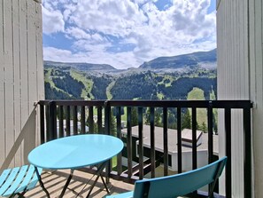 Een balkon met een tafel en stoelen, met uitzicht op een bergachtig landschap.