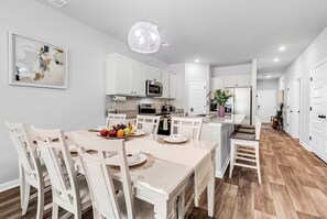 Une cuisine moderne avec des meubles blancs, une table à manger avec des chaises et un lustre.