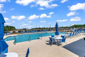 Un espace piscine avec des chaises et des parasols bleus, un ciel dégagé et une vue sur le paysage environnant.