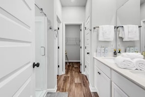 Une salle de bain moderne avec des meubles blancs, un plancher en bois et un miroir agrémenté de serviettes.