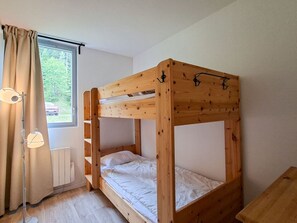 Ein Etagenbett mit Holzrahmen, ein Fenster mit Vorhängen und eine Stehlampe.