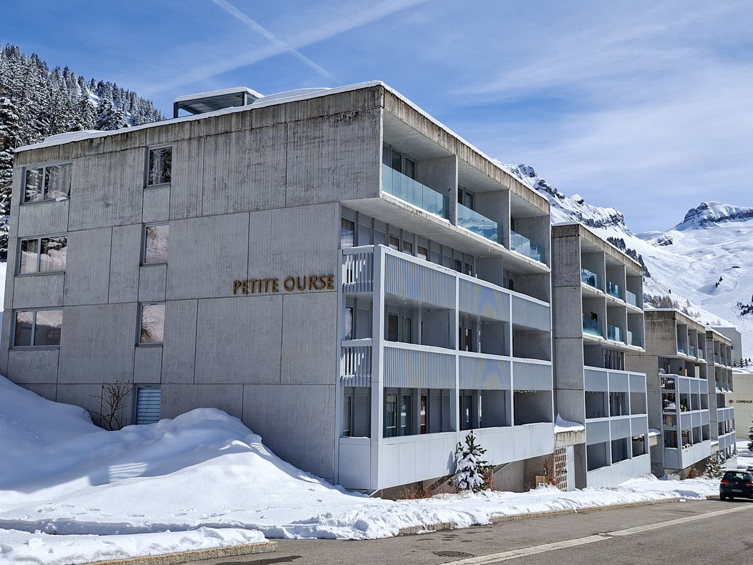 A multi-story building with a sign reading 'PETITE OURSE,' surrounded by snow and mountains.