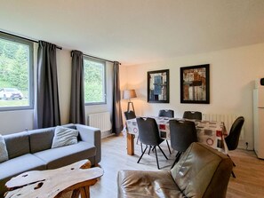 Ein modernes Wohnzimmer mit einer Couch, einem Ledersessel, einem Esstisch mit Stühlen und Kunstwerken an der Wand.
