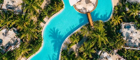 An aerial view of a resort with a large, winding pool surrounded by palm trees and resort buildings.