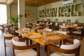 Un restaurante con varias mesas, sillas y una pared decorada con arte abstracto.