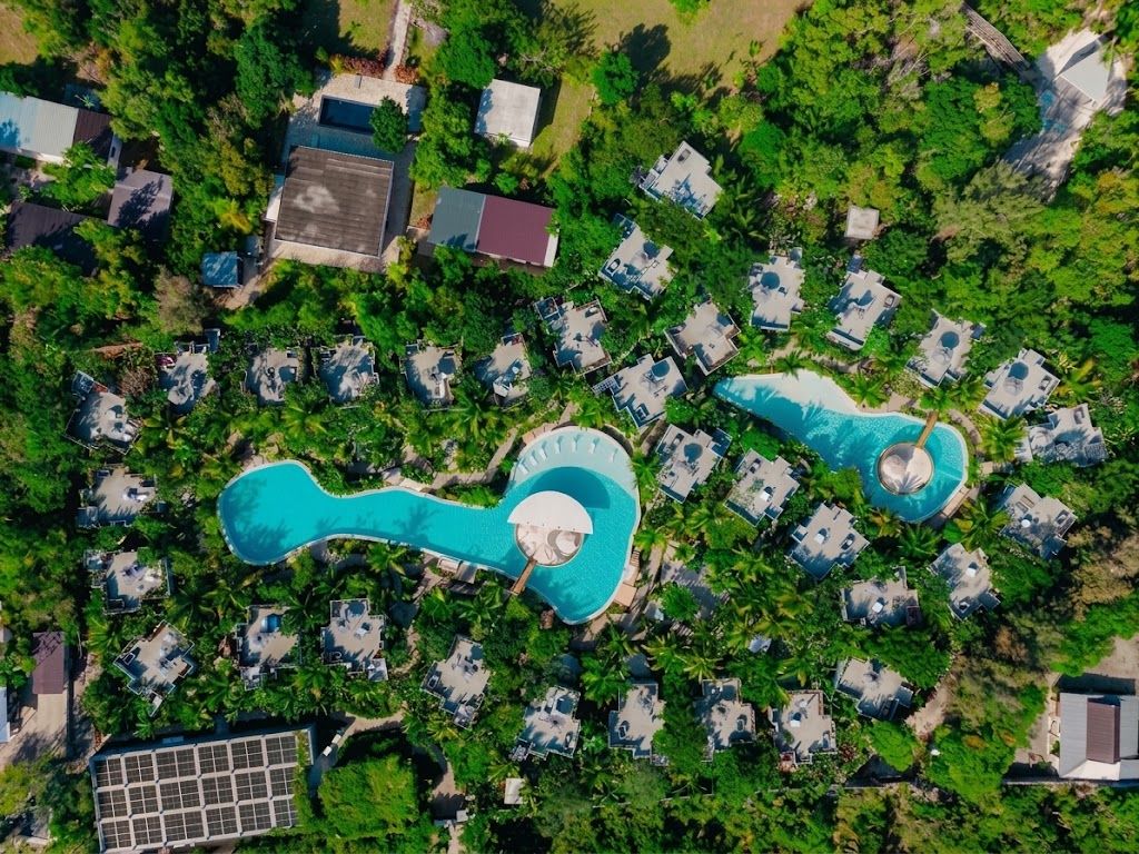 An aerial view of a resort with multiple bungalow-style accommodations, a central swimming pool, and surrounding greenery.
