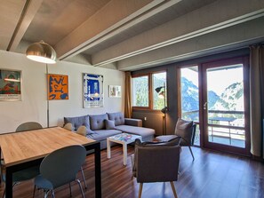 A modern living room with a wooden table, grey sofa, and a view of mountains through large windows. - Renovated apartment between slopes and shops - 6 guests (Flaine)