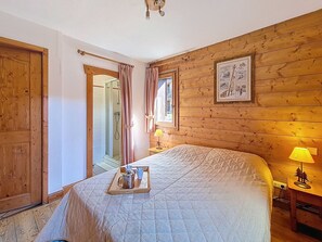 Ein Schlafzimmer mit Holzwand, einem Bett mit Quiltdecke, einem Nachttisch mit Lampe, einem Fenster mit Vorhängen und einer Tür.