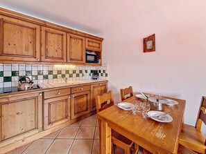 A kitchen with wooden cabinets, a tiled backsplash, and a dining table set for four. - Spacious apartment near the slopes - 4 guests (Les Menuires)