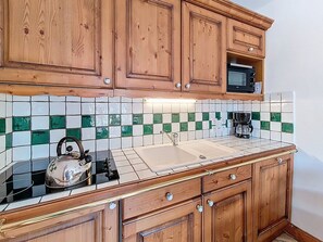 A kitchen with wooden cabinets, a tiled backsplash, a sink, a kettle, and a coffee maker. - Spacious apartment near the slopes - 4 guests (Les Menuires)