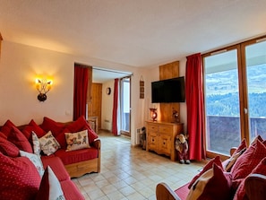 Ein gemütliches Wohnzimmer mit einer Couch, einem Fernseher und Blick ins Freie.