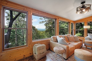A cozy cabin interior with large windows, a leather sofa, and a woven ottoman. - Tiny Pines - Ellijay, GA (Ellijay)