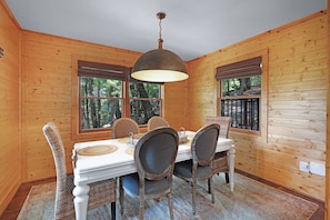 A wooden cabin dining room with a table set for four, large windows, and a hanging light fixture. - Tiny Pines - Ellijay, GA (Ellijay)