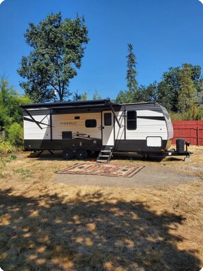 A recreational vehicle with a ramp for access, parked on a grassy area with a red fence in the background.