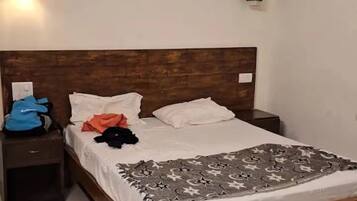 Ein Schlafzimmer mit einem Holzkopfteil, einem Bett mit einem gemusterten Überwurf, einem Nachttisch mit einer blauen Tasche und zwei Wandleuchten.