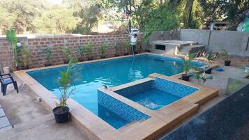 Ein rechteckiger Swimmingpool mit Fliesen, umgeben von einer Ziegelmauer und Topfpflanzen.