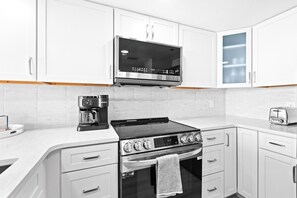 A modern kitchen with white cabinets, a stainless steel microwave, a coffee maker, a stove, and a toaster. - Vitamin Sea, Beachfront Condo, Gulf Views, Pool, Fire Pit (Santa Rosa Beach)