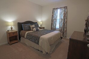 Ein Schlafzimmer mit einem Bett, Nachttischen, einer Kommode und einem Fenster mit Vorhängen.
