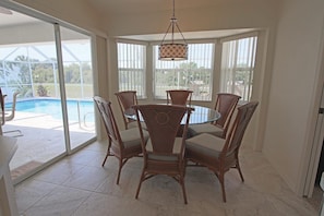A dining area with a round table and six chairs, large windows, and a view of a swimming pool. - Tranquil Retreat with Extended Lanai #313 (Rotonda West)