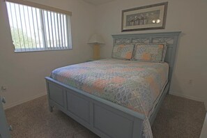 Een slaapkamer met een bed, een raam met jaloezieën, een lamp en een lijst met een foto aan de muur.