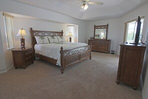 Ein Schlafzimmer mit einem hölzernen Bett, zwei Nachttischen, einer Kommode, einem Spiegel und einem Deckenventilator.