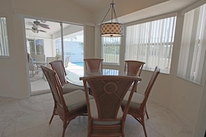 A dining area with a round table and wicker chairs, a ceiling fan, and a view of a pool through a glass door. - Tranquil Retreat with Extended Lanai #313 (Rotonda West)