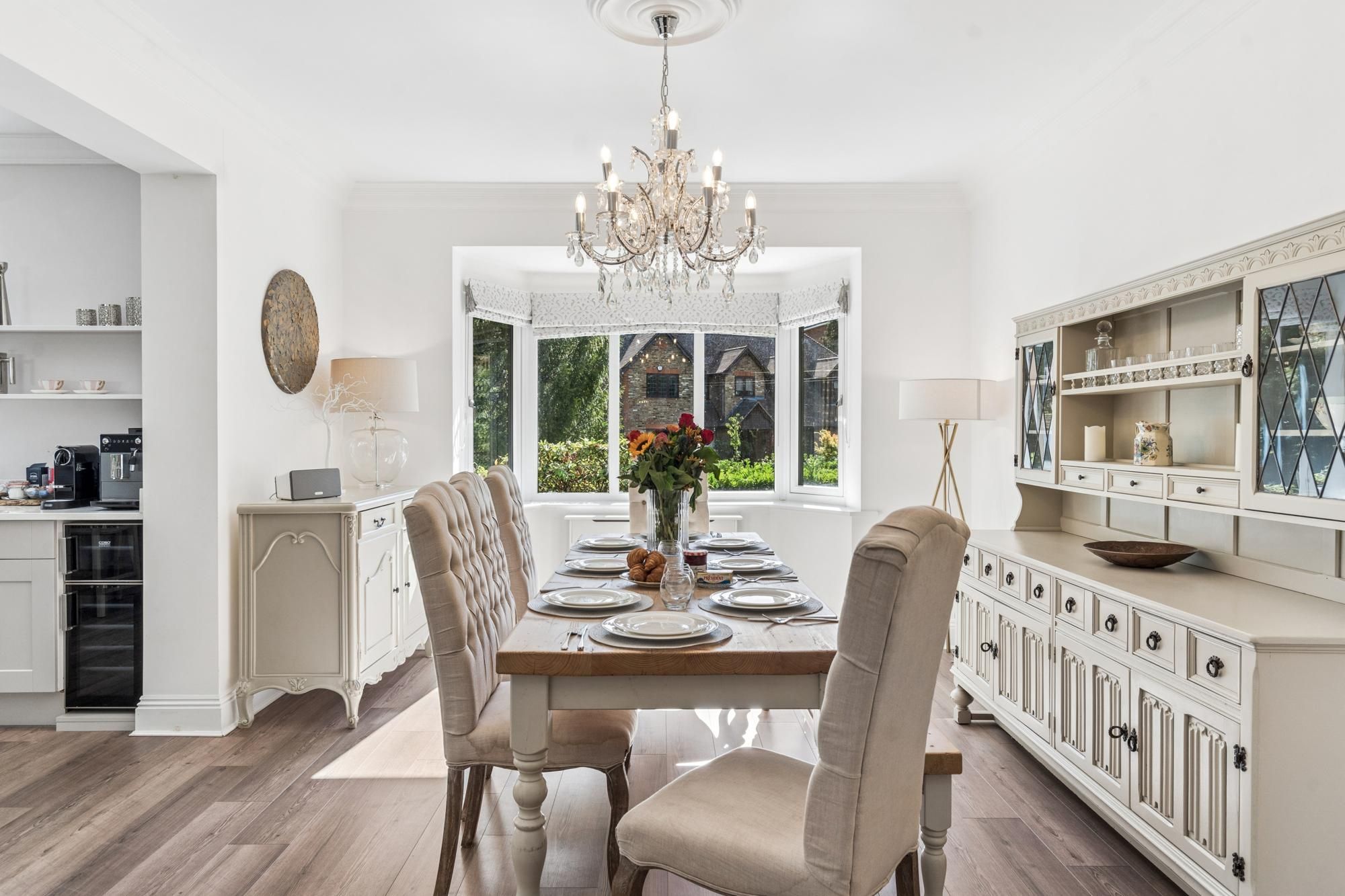 Ein Esszimmer mit einer Chandelier, Blick durch ein Erkerfenster und einer Küchenzeile mit Schränken.