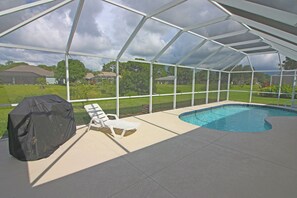 Ett takförsett utomhusområde med en swimmingpool, en grill och solstolar.