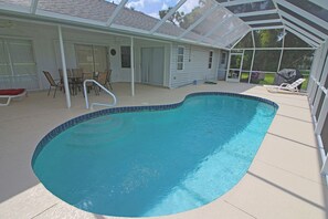 A swimming pool with a blue tiled edge, surrounded by a covered patio area with chairs and a table. - Waterfront Oasis: Rotonda West Canal #202 (Rotonda West)