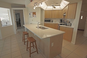 A kitchen with a central island, wooden cabinets, a microwave, and a ceiling fan. - Waterfront Oasis: Rotonda West Canal #202 (Rotonda West)
