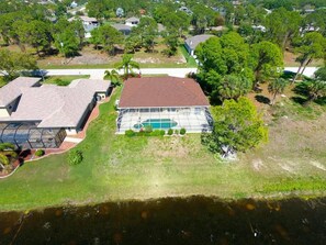 An aerial view of a residential property with a large swimming pool, a covered patio, and a well-maintained lawn. - Waterfront Haven: SW Facing Pool and Spa #10 (Rotonda West)