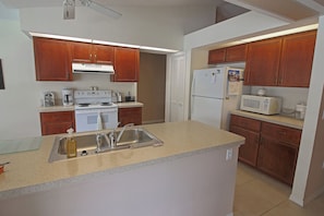A kitchen with wooden cabinets, a white stove, a sink, and a microwave. - Serene West Facing Pool -Rotonda West #15 (Rotonda West)