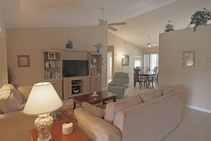 A living room with a sofa, a coffee table, a TV, and a lamp. There is a dining area with a table and chairs in the background. - Serene West Facing Pool -Rotonda West #15 (Rotonda West)