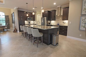 A modern kitchen with a central island, bar stools, dark cabinetry, stainless steel appliances, and pendant lighting. - Rotonda River Villa pool home #1125 (Rotonda West)
