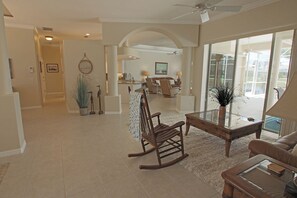 A spacious living area with a rocking chair, a glass coffee table, and a sofa. There is a kitchen in the background with a dining area. - Spacious Pool and Expansive Canal Views #811 (Rotonda West)