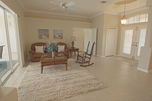A spacious living room with a brown sofa, a wooden coffee table, a rocking chair, and a large window. - Spacious Pool and Expansive Canal Views #811 (Rotonda West)