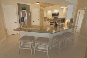 A kitchen with a central island, bar stools, stainless steel appliances, and a marble countertop. - Spacious Pool and Expansive Canal Views #811 (Rotonda West)