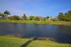 A serene lakeside view with a grassy area, a small pond, and several buildings with red roofs in the background. - Spacious Pool and Expansive Canal Views #811 (Rotonda West)