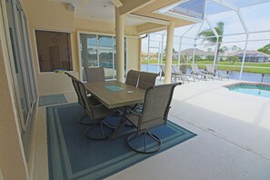 Un espace extérieur abrité où l’on peut prendre ses repas, avec une piscine en arrière-plan.