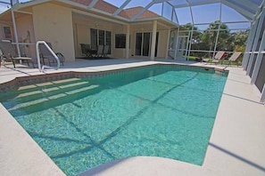 A swimming pool with clear water, surrounded by a covered patio area with chairs and a table. - Spacious Pool and Expansive Canal Views #811 (Rotonda West)